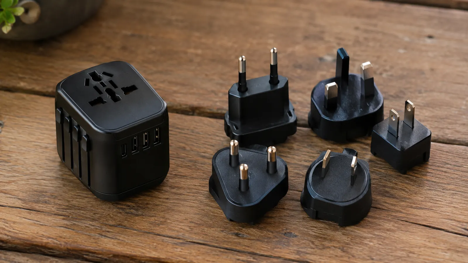 A small flat-lay of a universal travel adapter beside a handful of single-country plug adapters on a wooden table