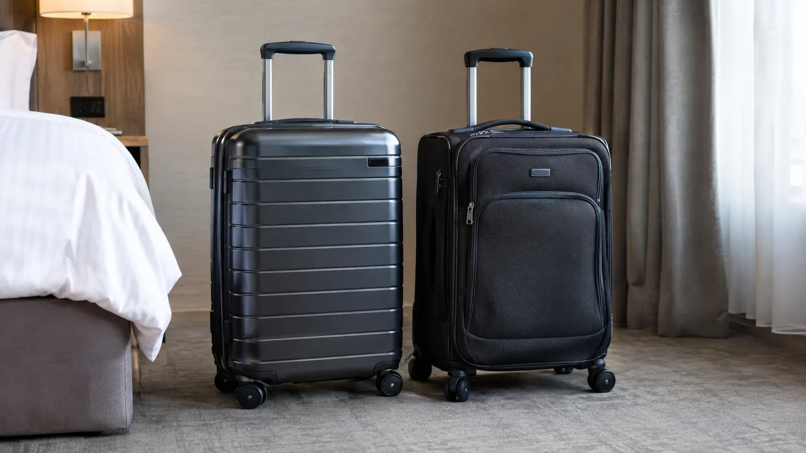 A hardside carry-on suitcase and a softside carry-on suitcase standing side by side in a hotel room