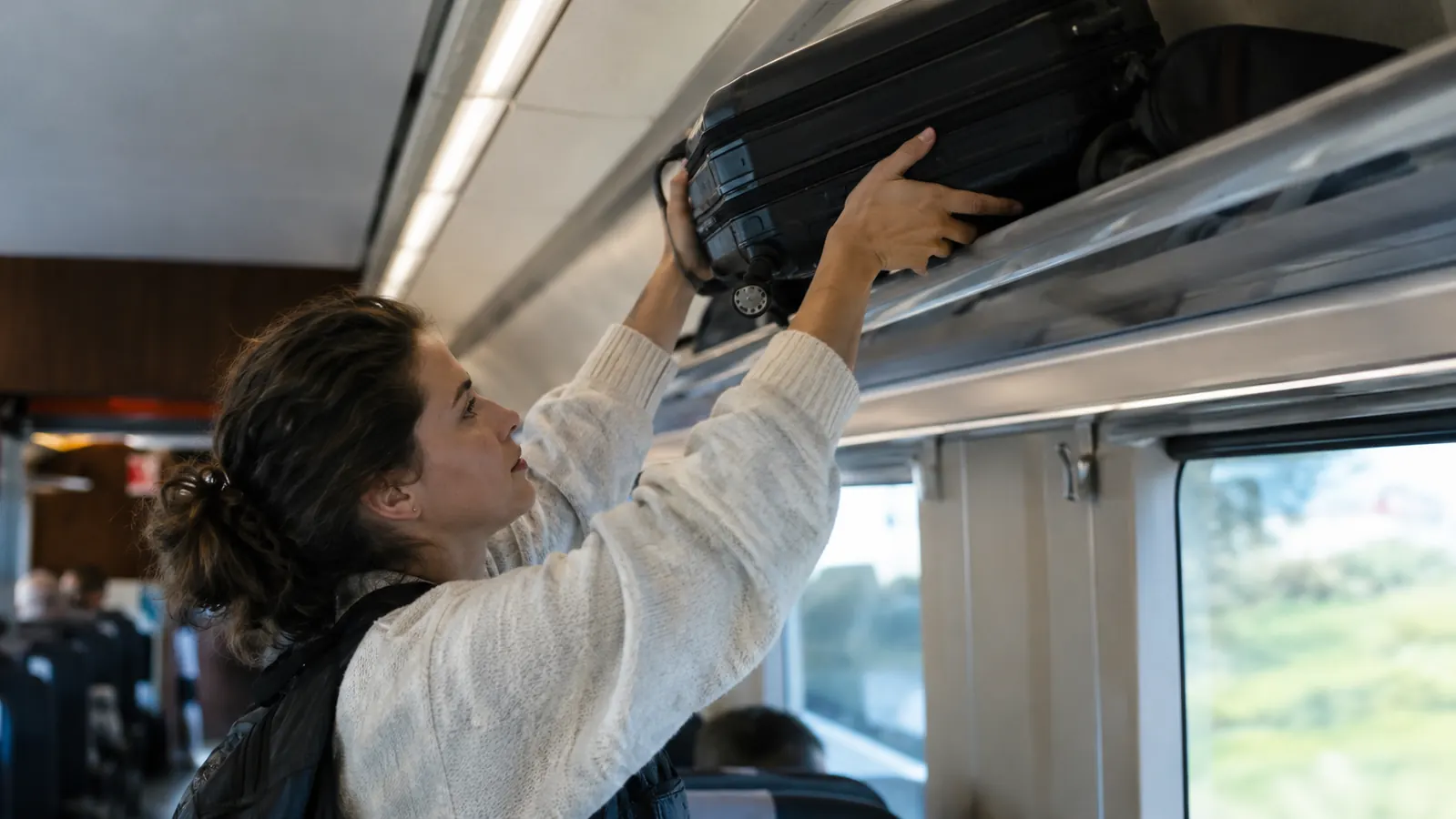 A traveler lifting a carry-on suitcase onto a train luggage rack